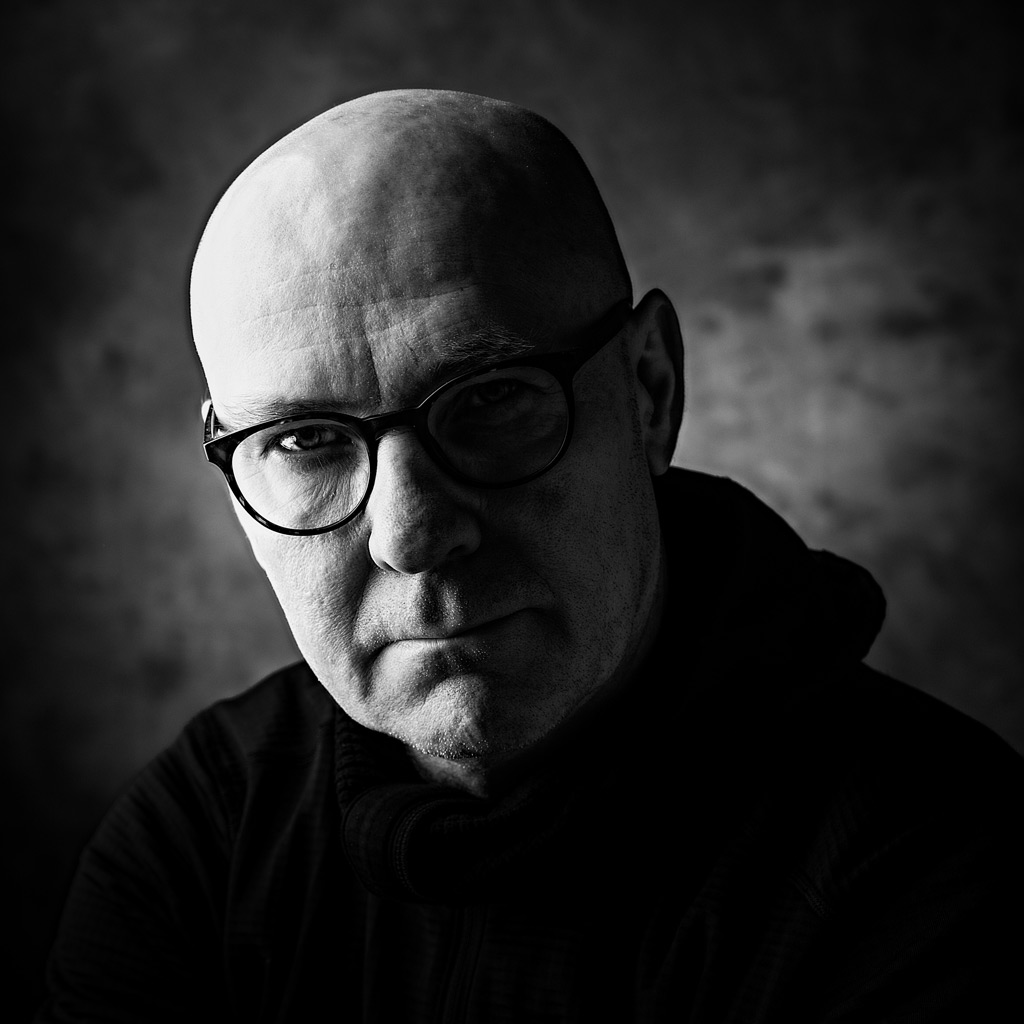 Kontrastikas mustavalkoinen muotokuva, mies silmälaseissa katsoo suoraan kameraan, Dragan-efekti.