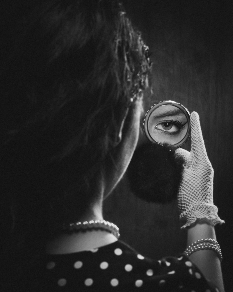 Henkilö poseeraa valkoisessa mekossa punaisen hirsiseinän edessä, kesäinen muotokuvaus.